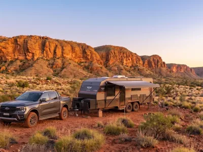 Australian made off road caravan parked at a remote camp at first light, red dirt and ochre gorges in the background, awning out